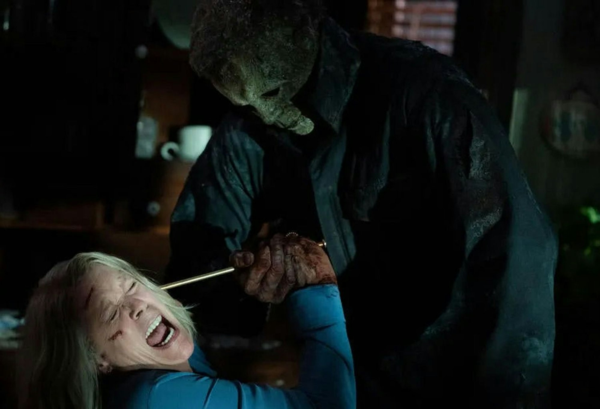 Michael Myers in dunkler Jacke geht mit einem spitzen Gegenstand auf Laurie alias Jamie Lee Curtis los. Sie schreit und wehrt sich.