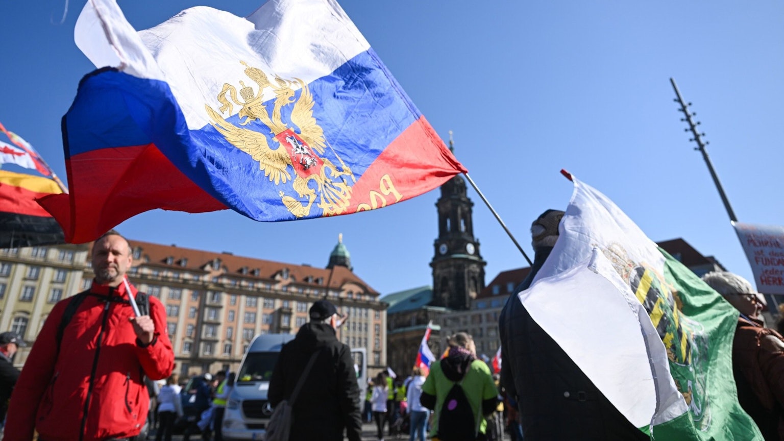 Teilnehmer einer Demonstration von Gegnern der Corona-Maßnahmen stehen in Dresden auf dem Altmarkt und halten eine Russland- und eine Sachsen-Fahne.