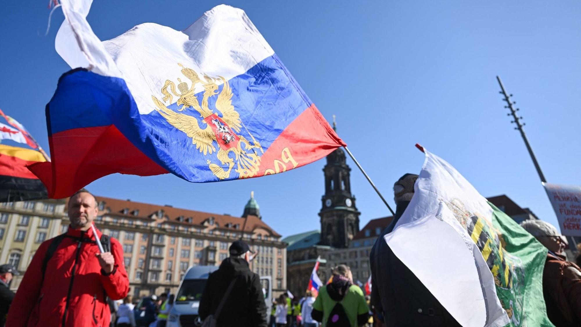 Teilnehmer einer Demonstration von Gegnern der Corona-Maßnahmen stehen in Dresden auf dem Altmarkt und halten eine Russland- und eine Sachsen-Fahne.