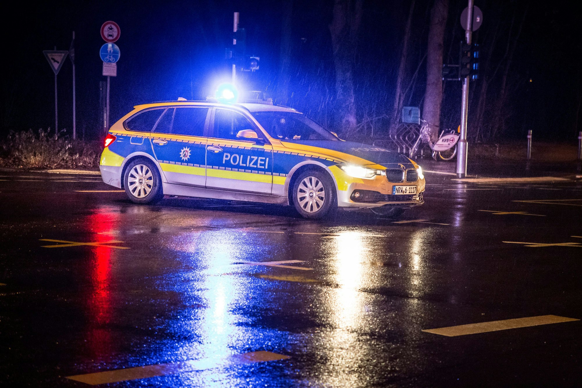 Ein Polizeiwagen mit eingeschaltetem Blaulicht auf einer regennassen Straßenkreuzung.