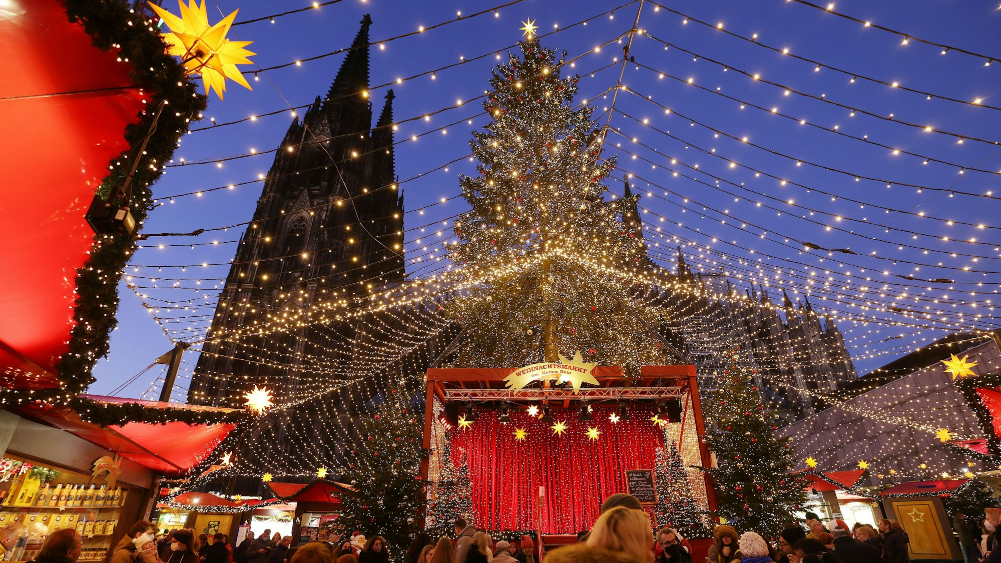 Besucher gehen über den Weihnachtsmarkt auf dem Roncalliplatz am Dom.