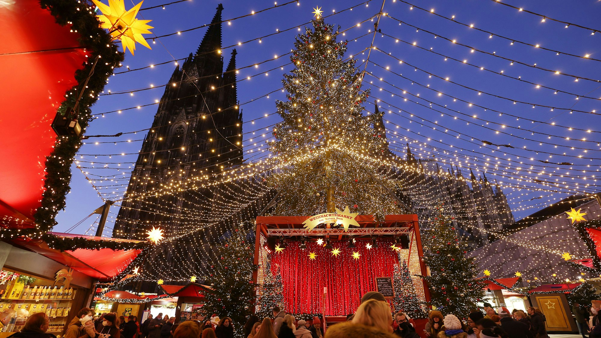 Besucher gehen über den Weihnachtsmarkt auf dem Roncalliplatz am Dom.