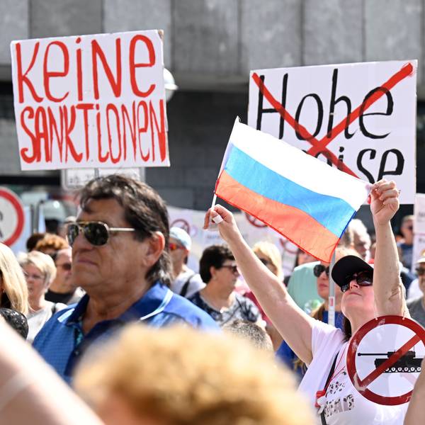Eine Teilnehmerin einer pro-russischen Kundgebung hält eine russische Fahne hoch, andere Schilder auf denen durchgestrichene Panzer und die Worte "Keine Sanktionen" stehen.