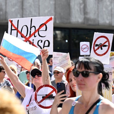 Eine Teilnehmerin einer pro-russischen Kundgebung hält eine russische Fahne hoch, andere Schilder auf denen durchgestrichene Panzer und die Worte "Keine Sanktionen" stehen.