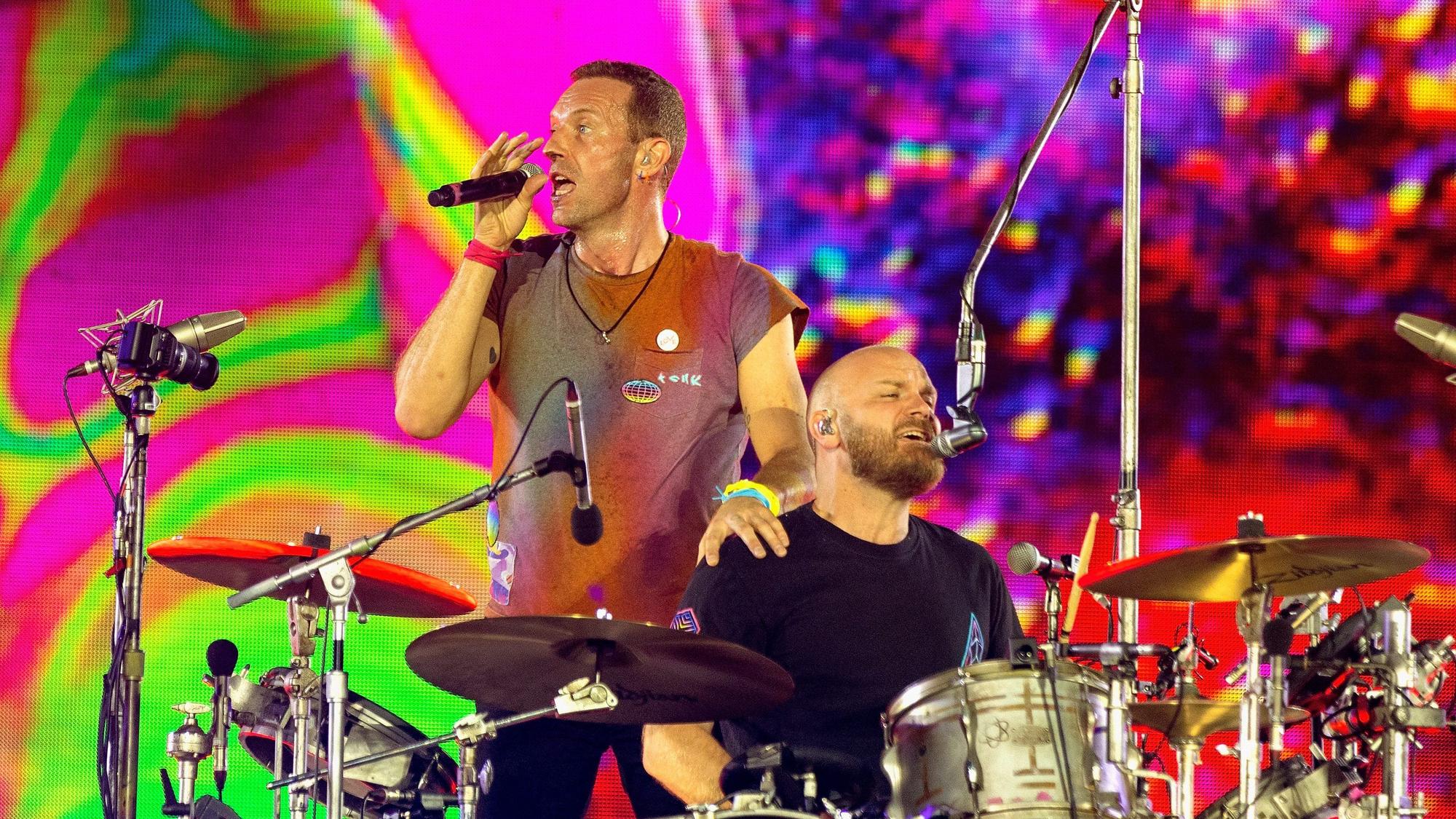 Chris Martin (l), Sänger von Coldplay, steht neben Will Champion, dem Schlagzeuger der Band auf der Bühne des Wembley-Stadions im Norden Londons. Hinter ihnen ist eine bunte Lichter-Show.