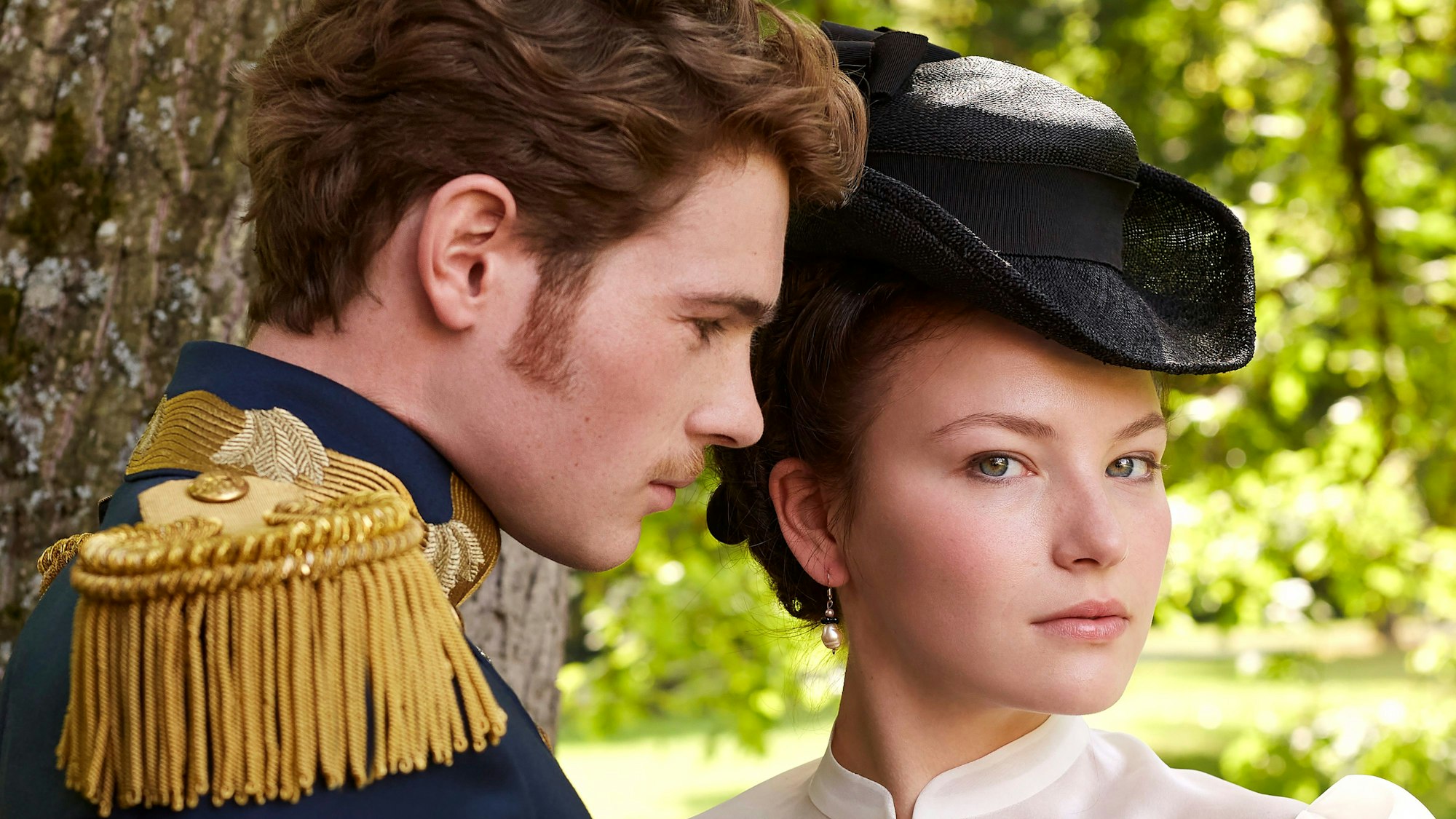 Sisi (Devrim Lingnau, r) und Franz (Philip Froissant) in einer Szene aus „Die Kaiserin“ (undatierte Aufnahme). Sie stehen in der Natur nah nebeneinander. Sisi guckt in die Kamera und Franz schaut sie an.