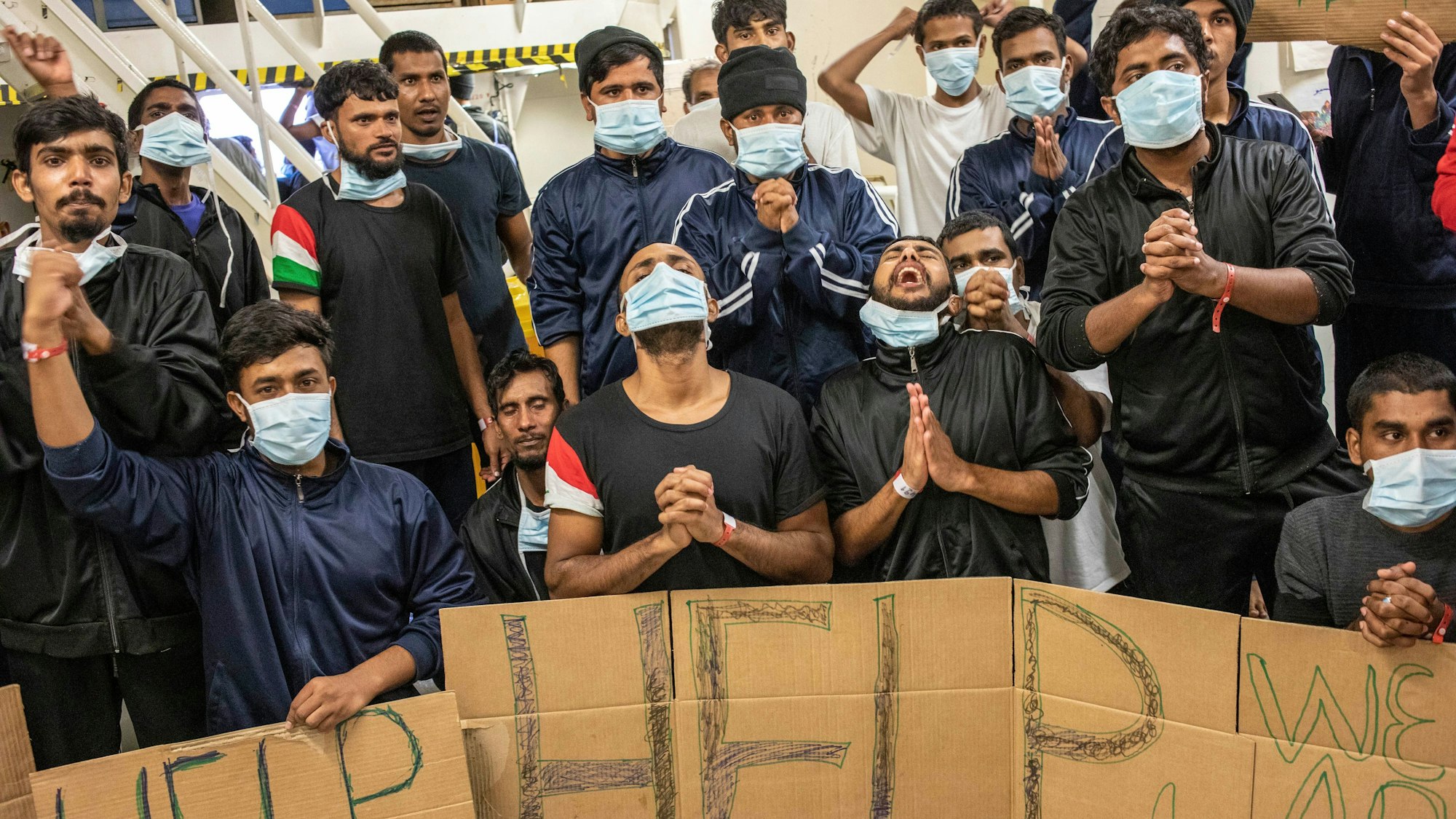 7.11.2022, Italien, Catania: Migranten halten Plakate, auf denen sie die Ausschiffung für alle fordern, während sie an Bord des unter norwegischer Flagge fahrenden Rettungsschiffs Geo Barents warten.