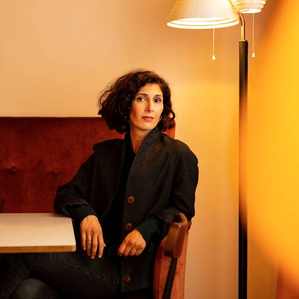 Nava Ebrahimi sitzt auf einem roten Sofa vor einer Stehlampe