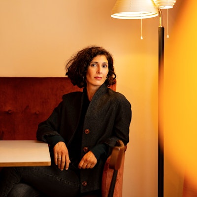 Nava Ebrahimi sitzt auf einem roten Sofa vor einer Stehlampe