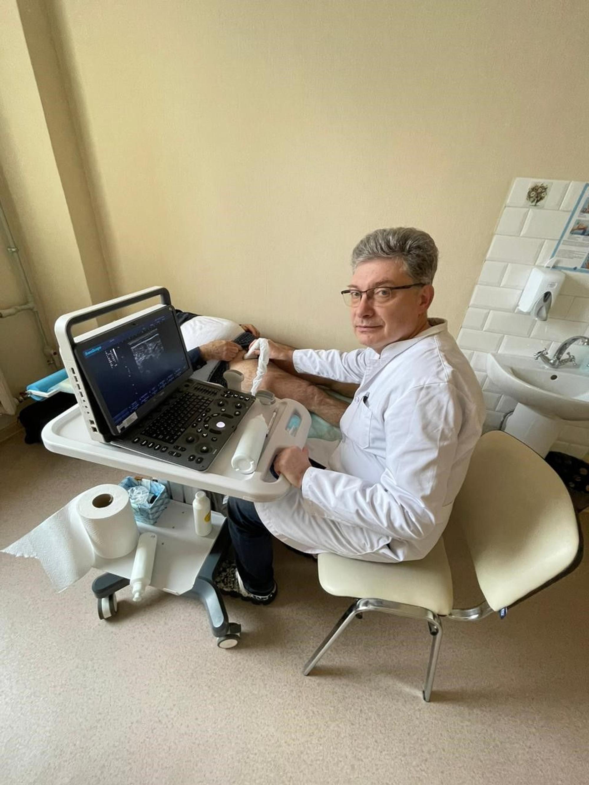 Gefäßchirurg Dr. Vitaliy P. sitzt vor dem neuen Gefäßultraschallgerät, und wendet dieses am Bein eines Patienten an, der vor ihm auf einer Liege liegt.
