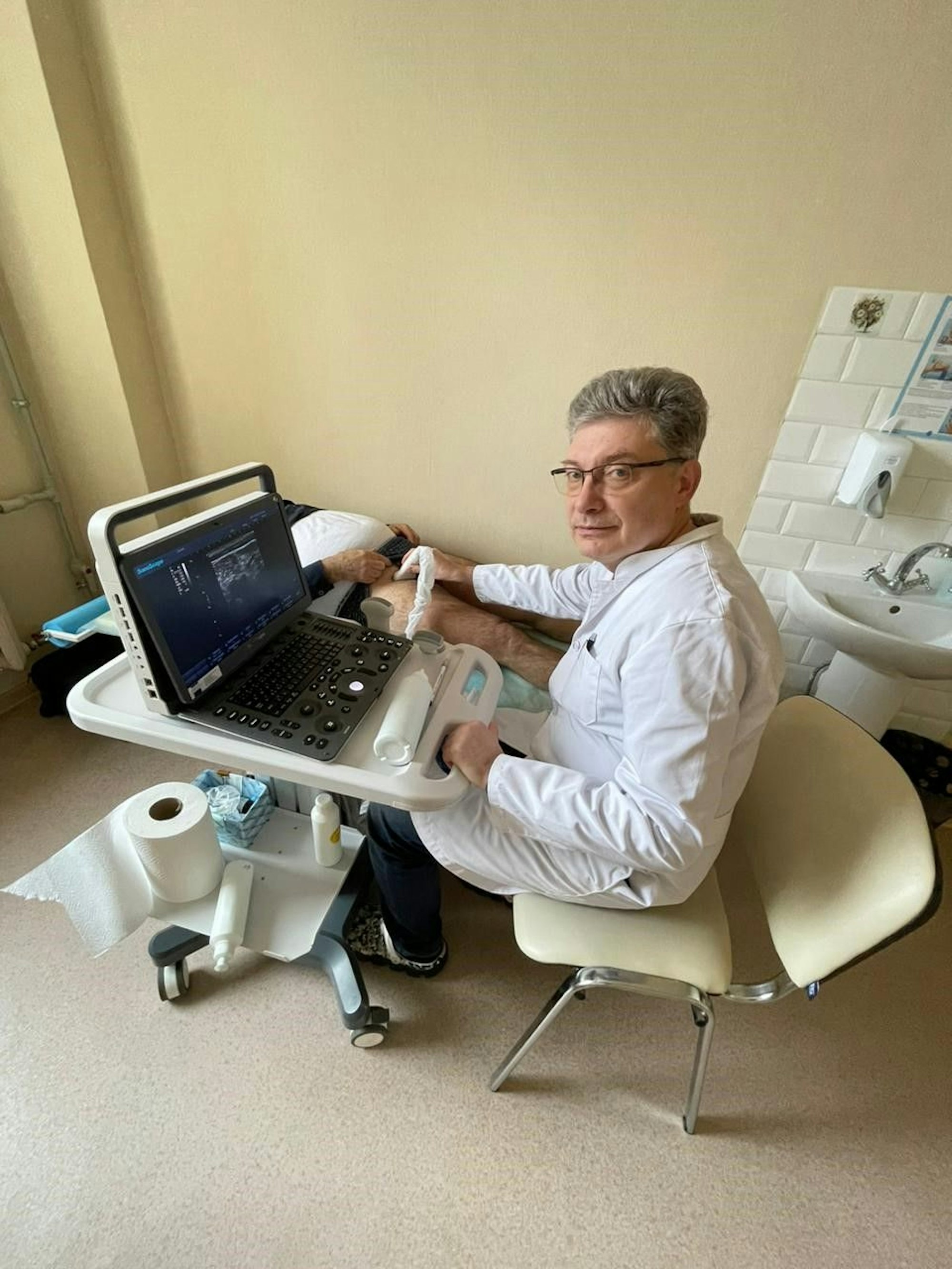 Gefäßchirurg Dr. Vitaliy P. sitzt vor dem neuen Gefäßultraschallgerät, und wendet dieses am Bein eines Patienten an, der vor ihm auf einer Liege liegt.