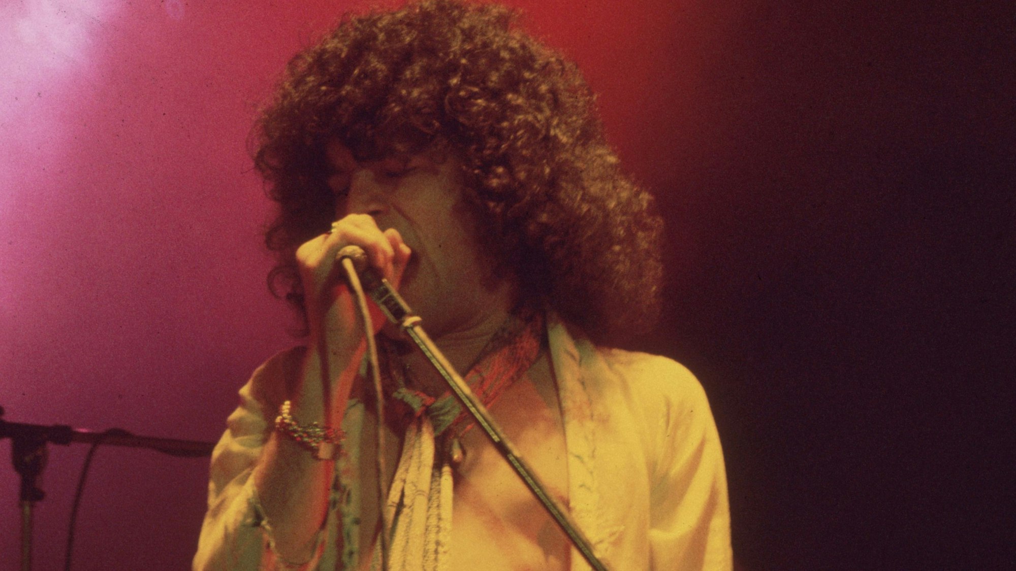 Dan McCafferty von Nazareth singt in ein Mikrofon. Er hat eine Lockenmähne und trägt ein gelbes, offenes Hemd.