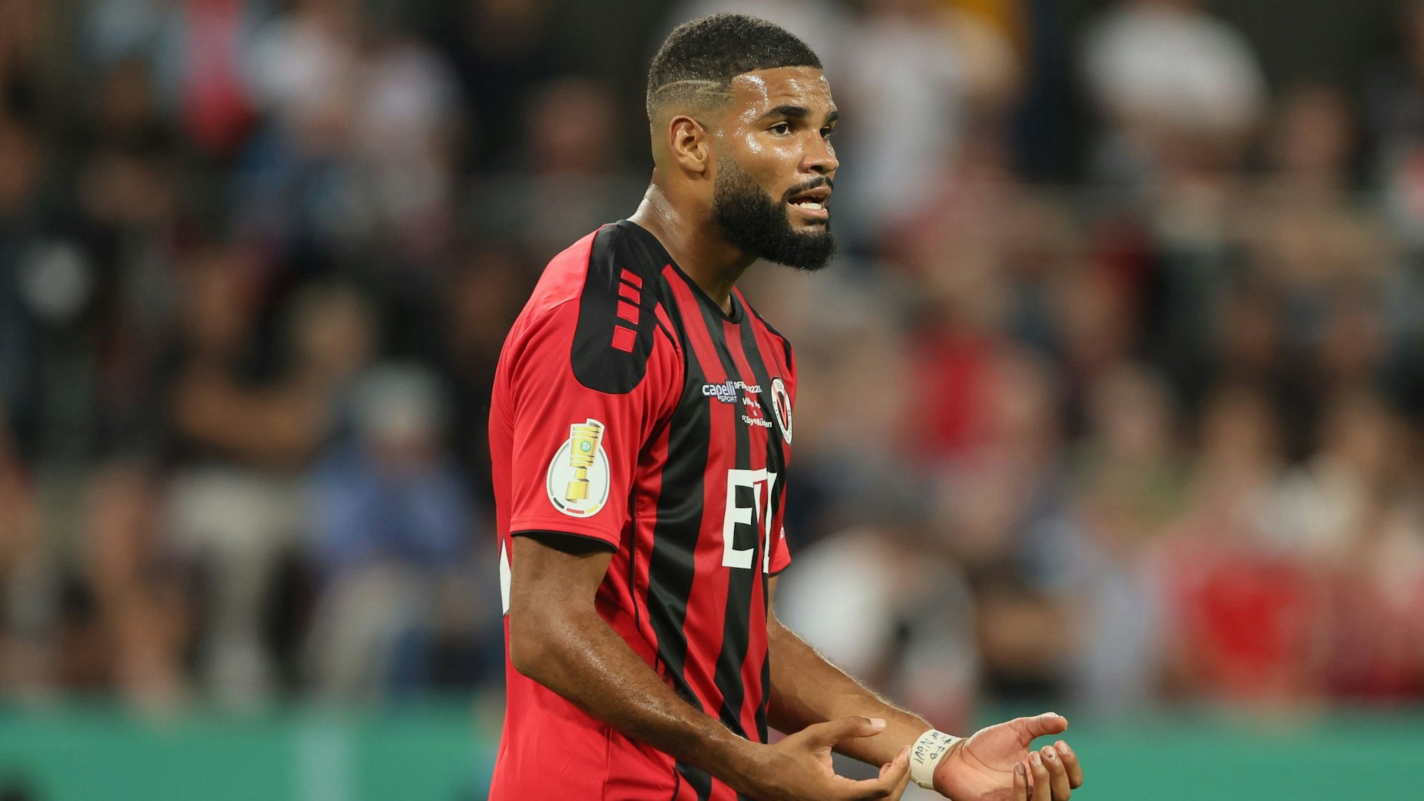 Ein Fußballspieler steht im Stadion und hält die Hände vor dem Körper.