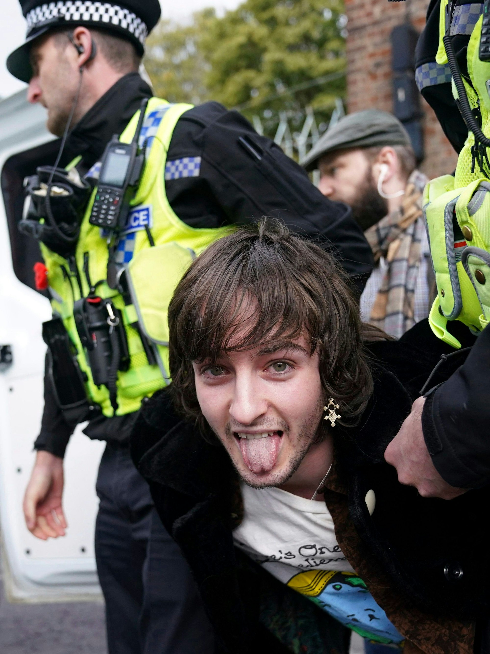 Ein Demonstrant, der Eier auf König Charles III. und Königsgemahlin Camilla geworfen hat, wird von zwei Beamten festgehalten. Währenddessen streckt er die Zunge in die Kamera.