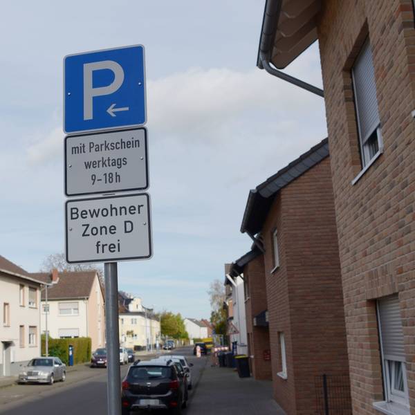 Ein Parken-Verkehrsschild steht auf einer Straße. Die Bewohner der Zone D können kostenfrei parken. Mehrere Autos stehen geparkt am Straßenrand.