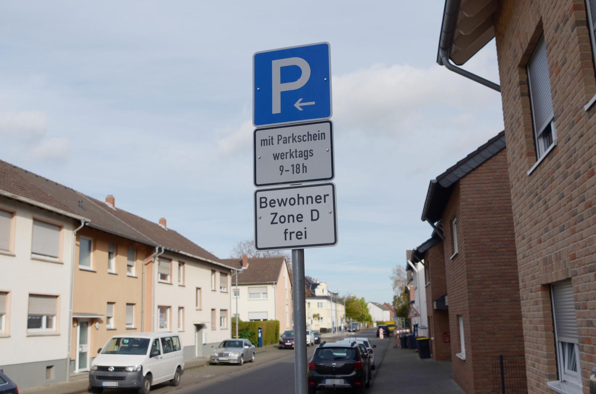 Ein Parken-Verkehrsschild steht auf einer Straße. Die Bewohner der Zone D können kostenfrei parken. Mehrere Autos stehen geparkt am Straßenrand.
