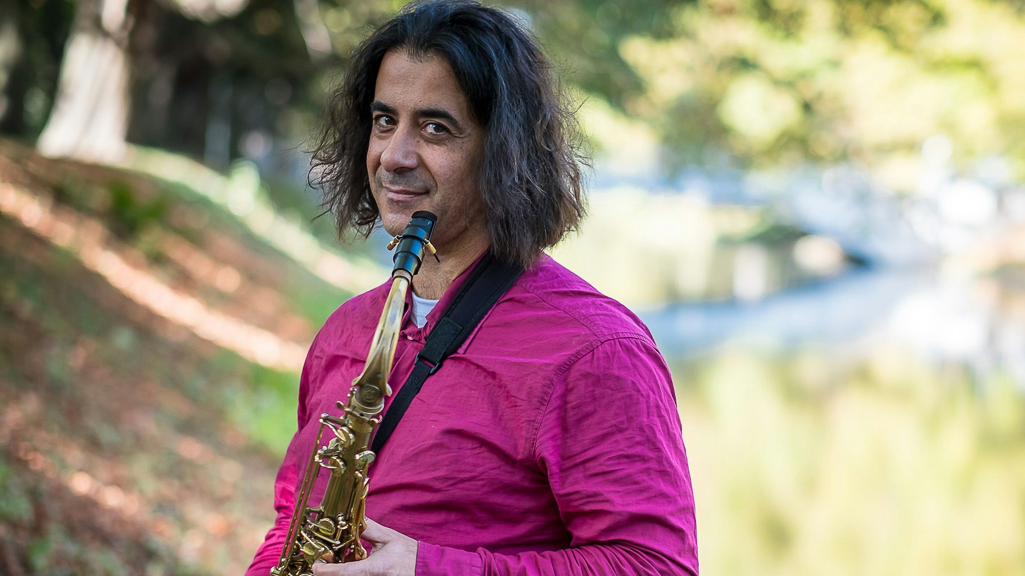 Ein Mann mit einem Saxofon steht an einem Kanal im Sonnenschein.