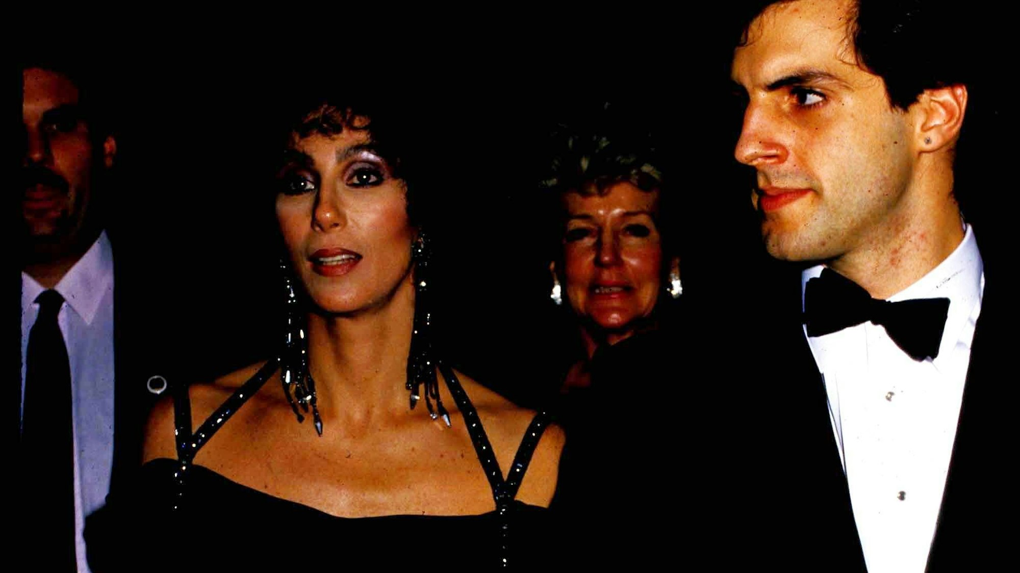 Cher und Rob Camilletti Arm in Arm, beide tragen Schwarz. Sie ein schulterfreies Kleid mit Glitzer. Er einen Anzug und weißes Hemd mit Fliege.