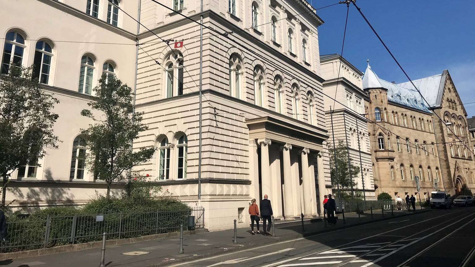Außenansicht vom Landgericht Bonn. Bei schönem Wetter gehen vor dem Gebäude mehrere Personen spazieren.