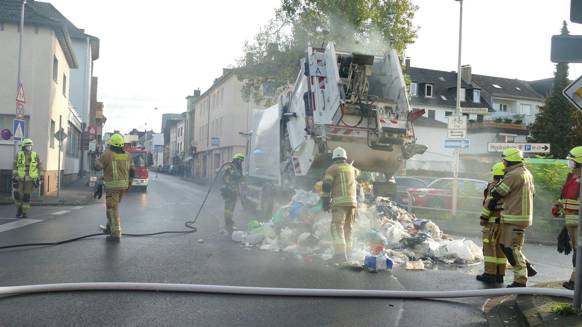 Feuerwehrleute löschen einen brennenden Müllwagen, der den Abfall auf die Straße entlädt.