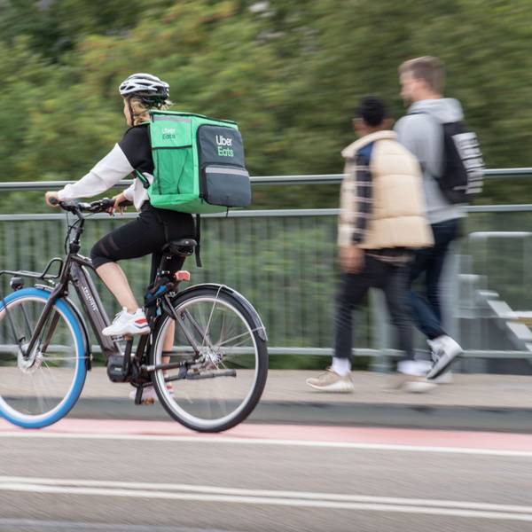 Eine Radfahrerin trägt einen grünen Rucksack von Uber Eats und fährt auf einem Radweg über eine Brücke.