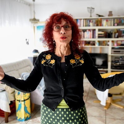 Shulamit Grohmann steht in ihrem Wohnzimmer, spitzt den Mund und hebt die Hände.