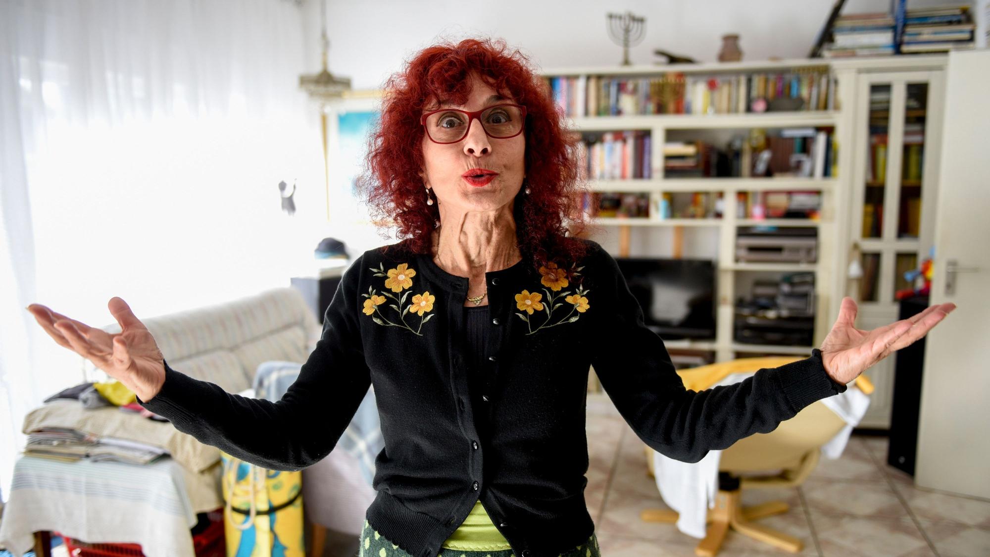 Shulamit Grohmann steht in ihrem Wohnzimmer, spitzt den Mund und hebt die Hände.