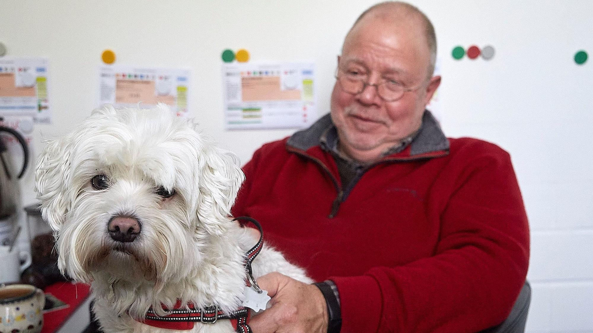 Rolf Zimmermann sitz auf einem Stuhl und hat einen Hund auf dem Schoß.