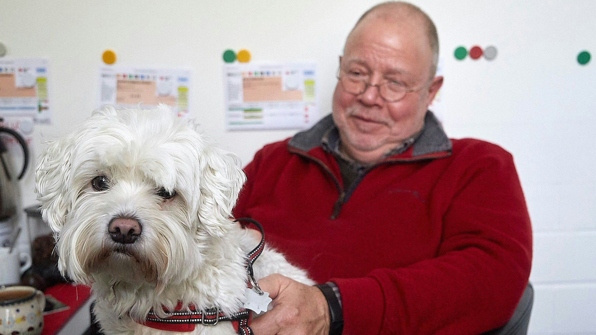 Rolf Zimmermann sitz auf einem Stuhl und hat einen Hund auf dem Schoß.