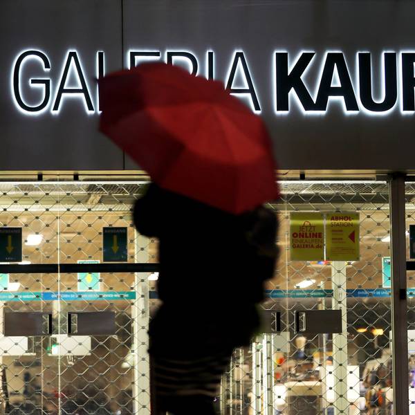 Eine Frau geht mit Regenschirm an einer geschlossenen Kaufhof Filiale vorbei.
