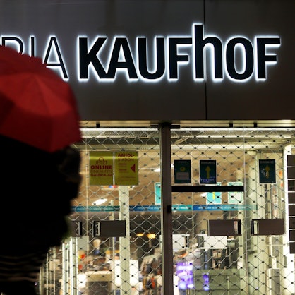 Eine Frau geht mit Regenschirm an einer geschlossenen Kaufhof Filiale vorbei.