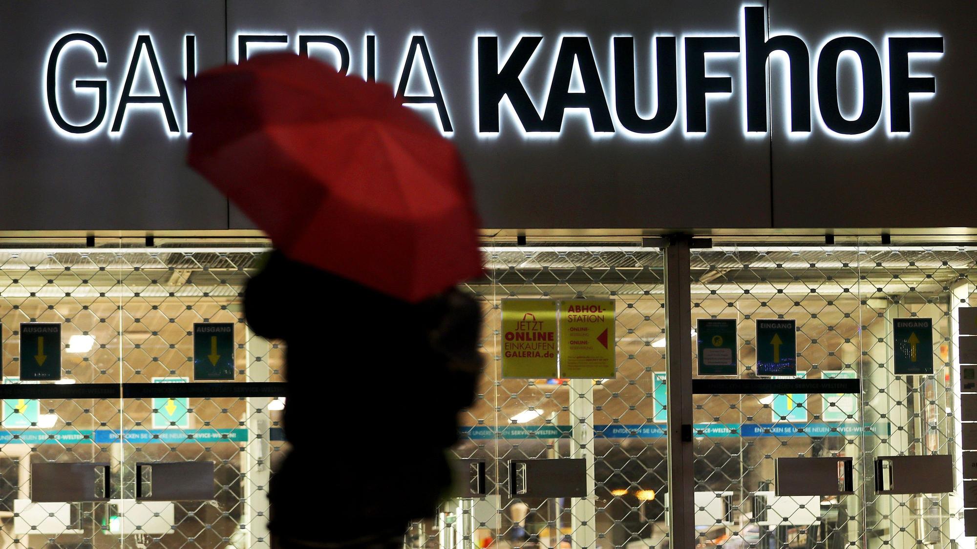 Eine Frau geht mit Regenschirm an einer geschlossenen Kaufhof Filiale vorbei.