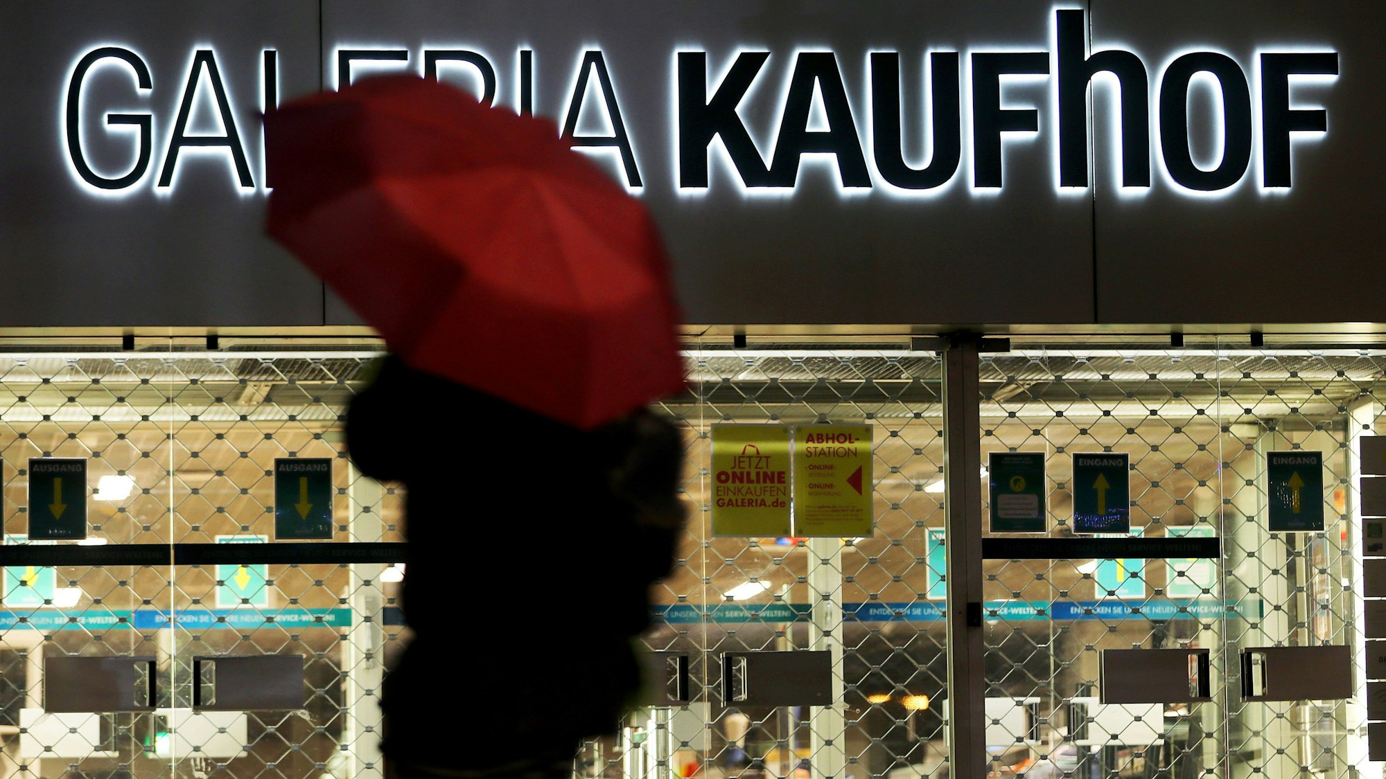 Eine Frau geht mit Regenschirm an einer geschlossenen Kaufhof Filiale vorbei.