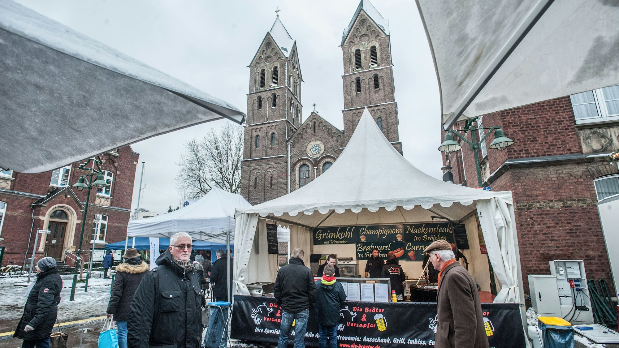 Vor der Schlebuscher St. Andreas Kirche steht ein Grünkohl-Stand, es hat geschneit.
