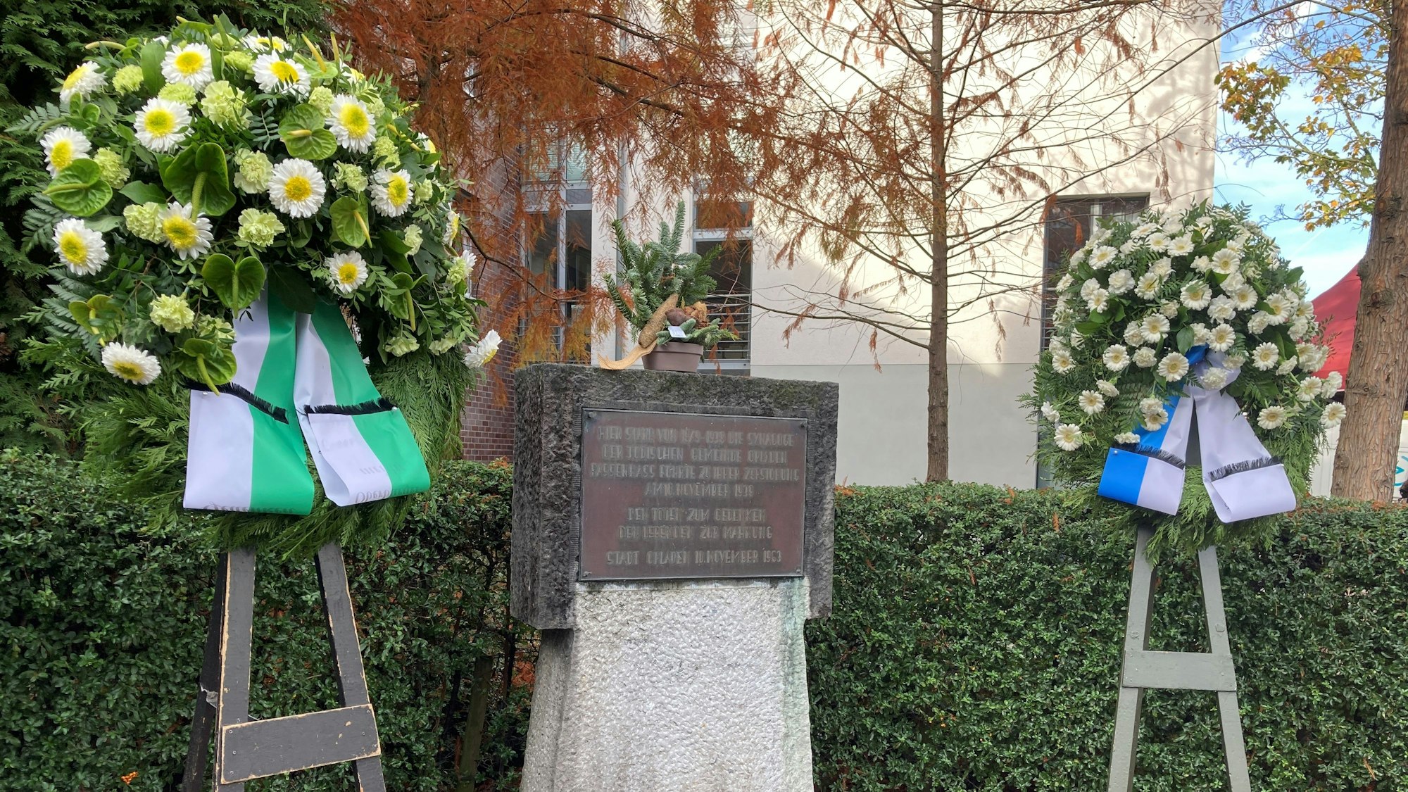 Zwei Blumenkränze stehen neben der Gedenktafel am Platz der Synagoge in Opladen.