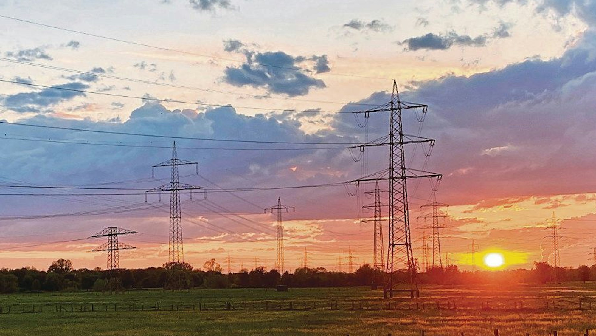 Sonnenuntergang im Mai, der Himmel ist blau, rot und gelb gefärbt. Davor stehen Strommasten.