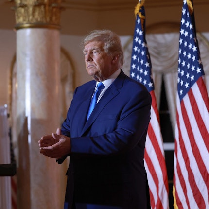 Ex-US-Präsident Donald Trump am Abend der Midterm-Wahlen in seiner Residenz in Mar-a-Lago. Trump steht vor drei US-amerikanischen Nationalflaggen und klatscht.