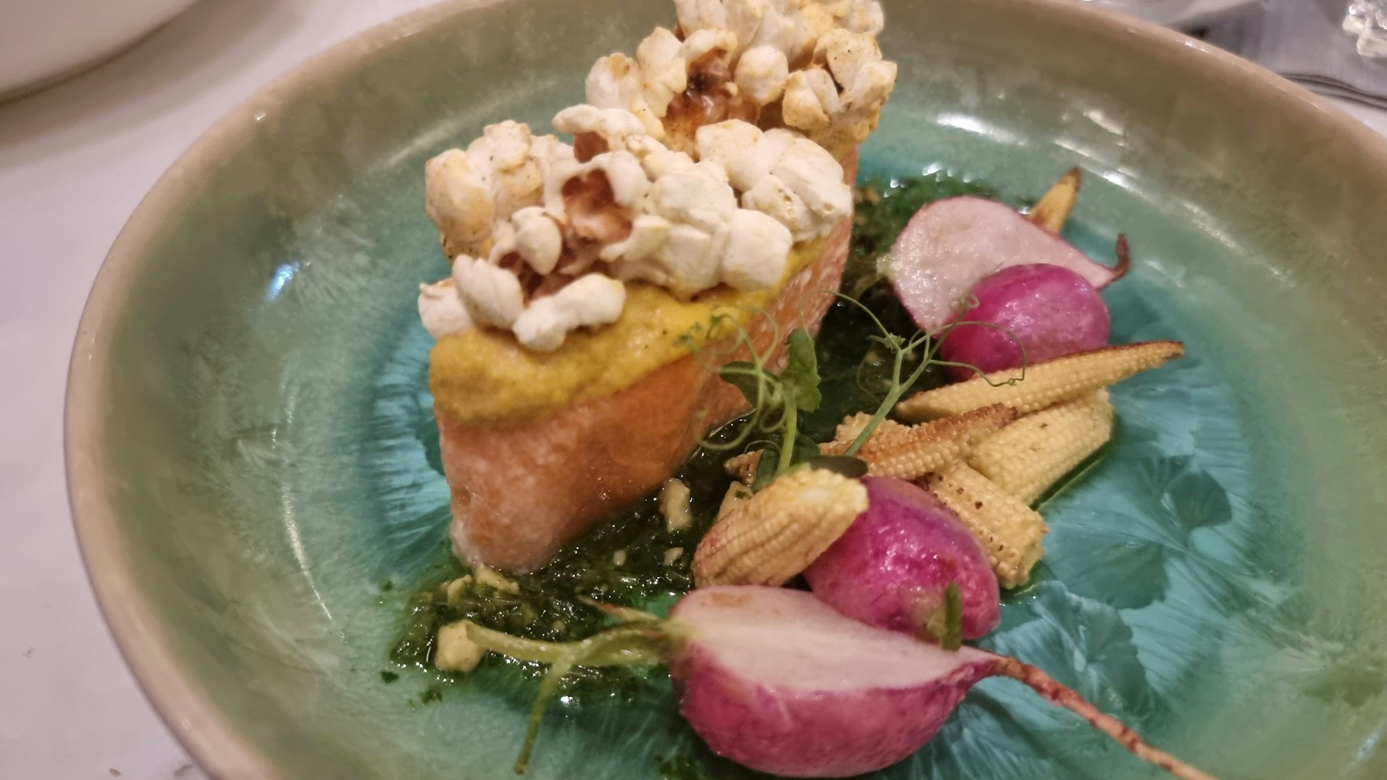 Teller mit confiertem Lachs, Radieschen, kleinen Maiskolben und Popcorn.