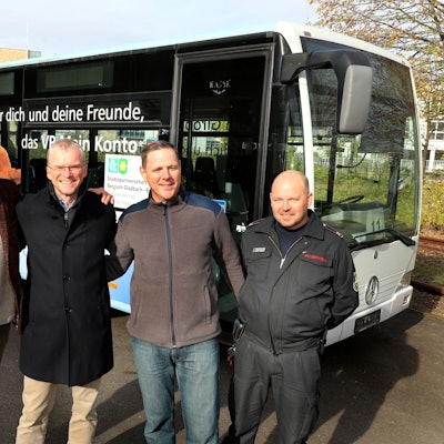 Fünf beteiligte Männer der Städtepartnerschaft Bergisch Gladbach-Butscha stehen Arm in Arm vor einem Bus.