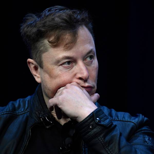 Elon Musk sitzt auf einer Bühne und wird in der Nahaufnahme gezeigt.