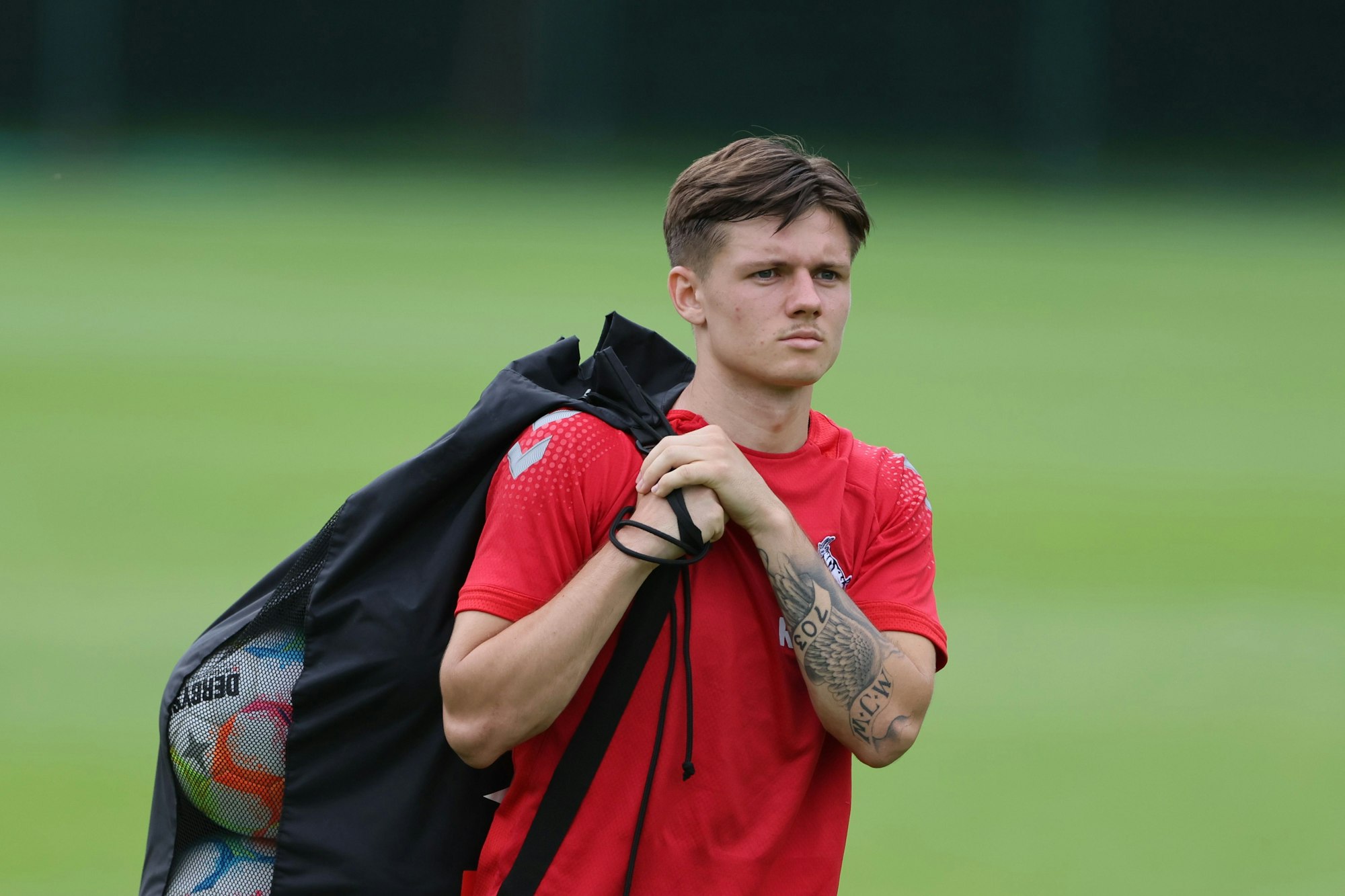 Ein Fußballspieler befindet sich mit einer Tasche voller Bälle über der Schulter auf dem Weg zum Training.