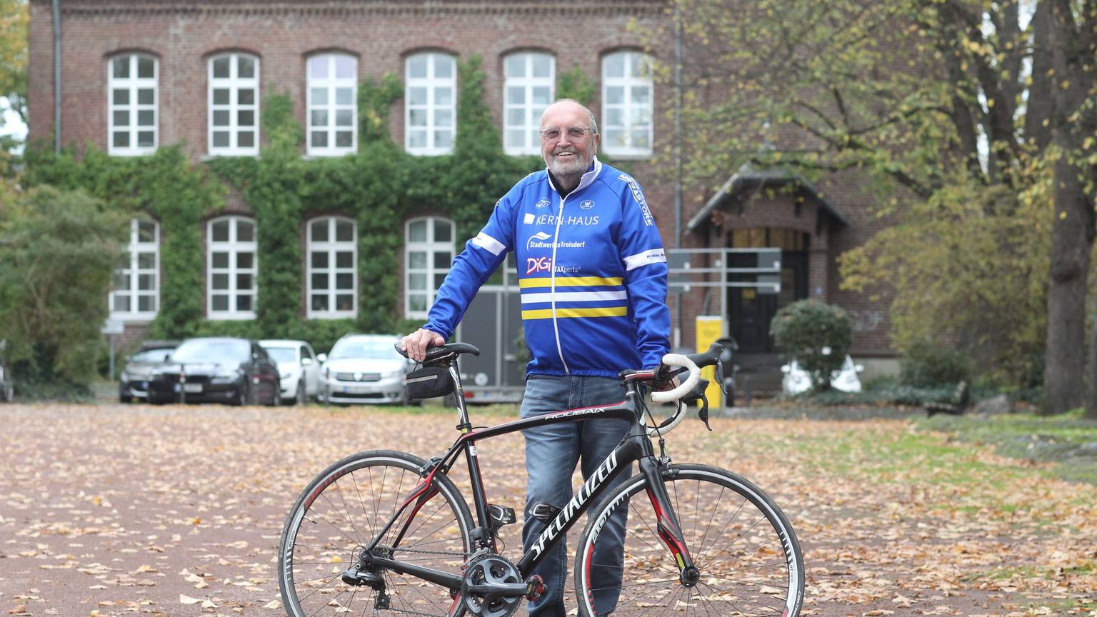 Radsportfunktionär Helmut Elfgen steht mit seinem Rad vor einem Gebäude.