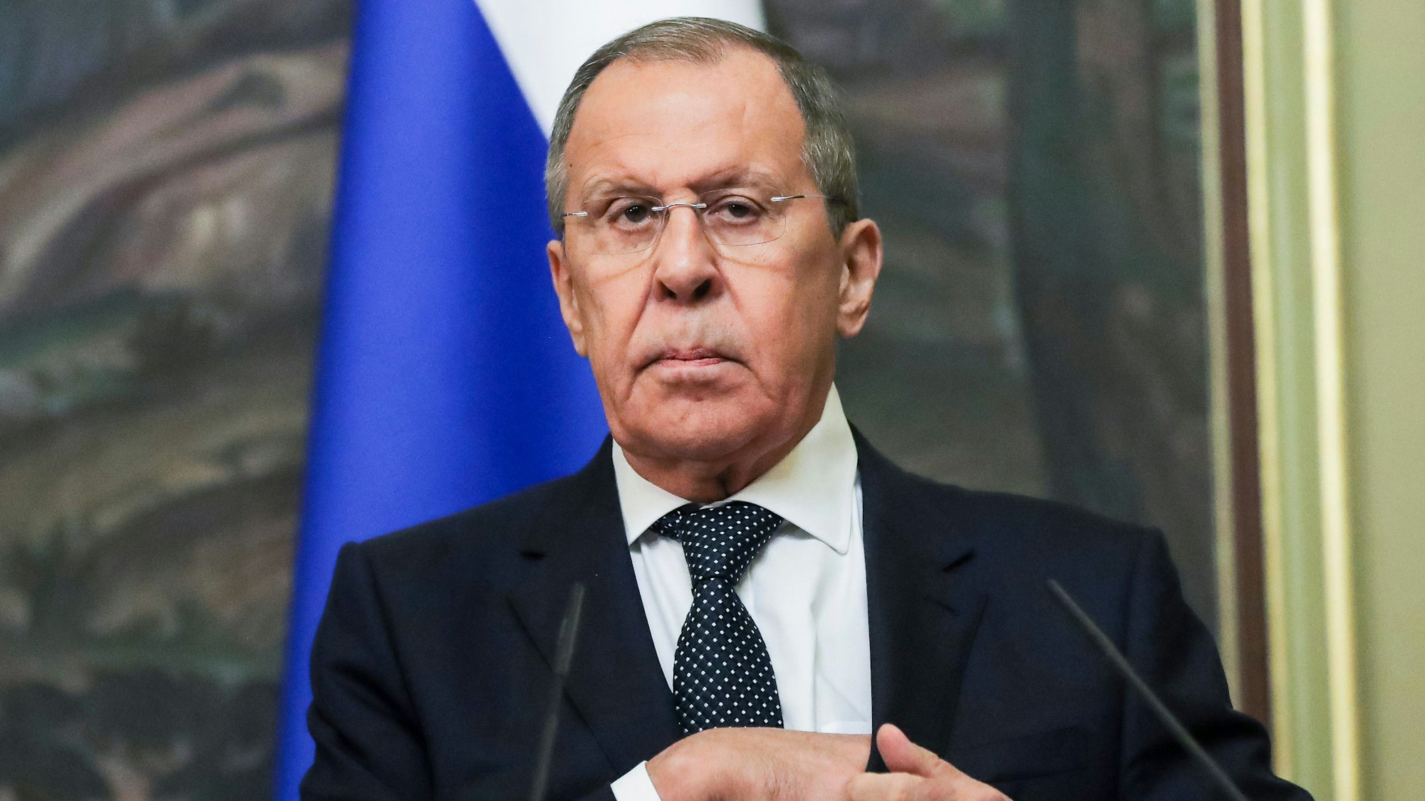 Russlands Außenminister Sergej Lawrow steht im Anzug vor Mikrofonen, er blickt missmutig, im Hintergrund hängt eine russische Flage.
