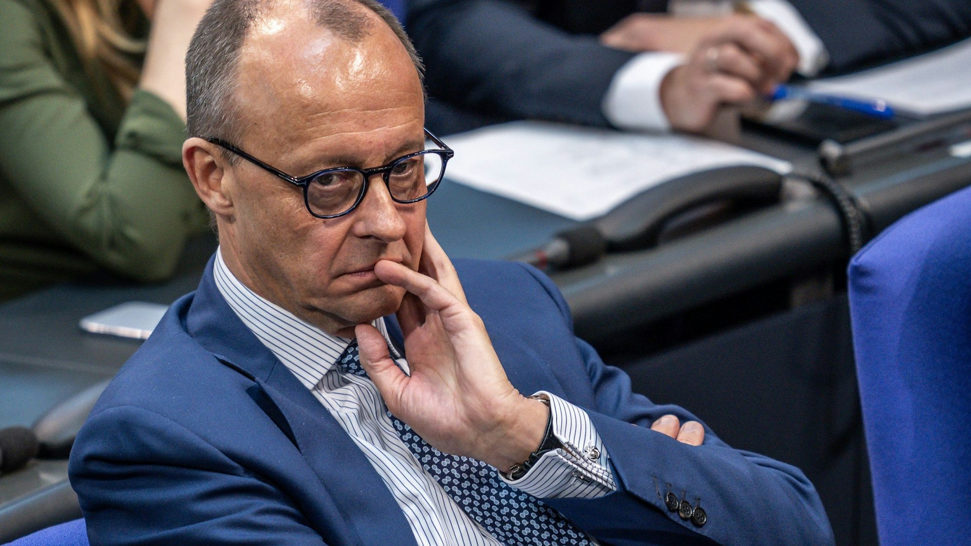 Friedrich Merz sitzt im Bundestag und hört einer Rede zu.