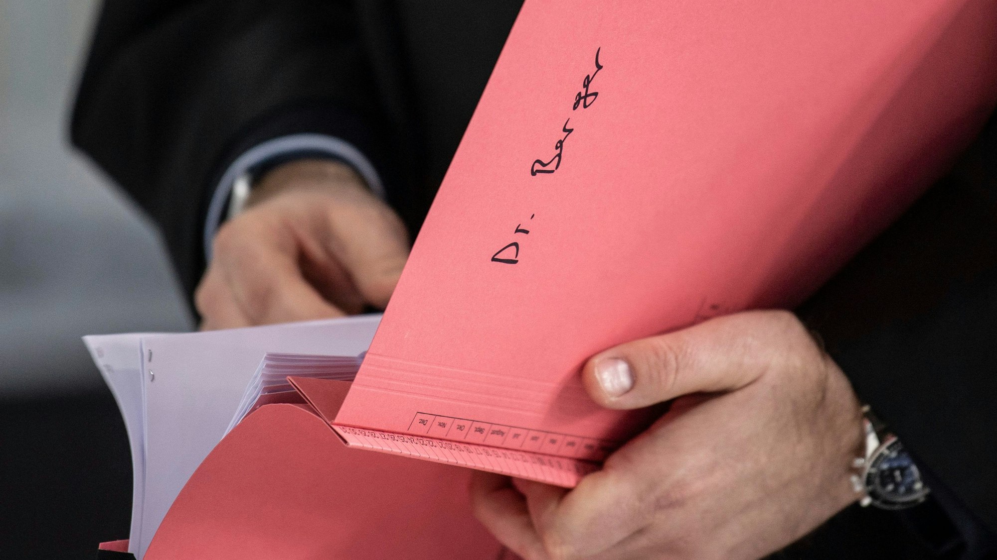 Ein Rechtsanwalt in schwarzer Robe mit einer rötlichen Prozessakte.