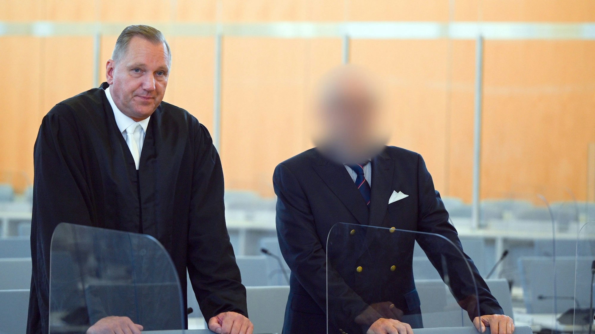 Ein Angeklagter steht mit seinem Verteidiger Christopher Hilgert vor Beginn des Prozesses im Gerichtssaal. Der Angeklagte wurde aus rechtlichen Gründen gepixelt.