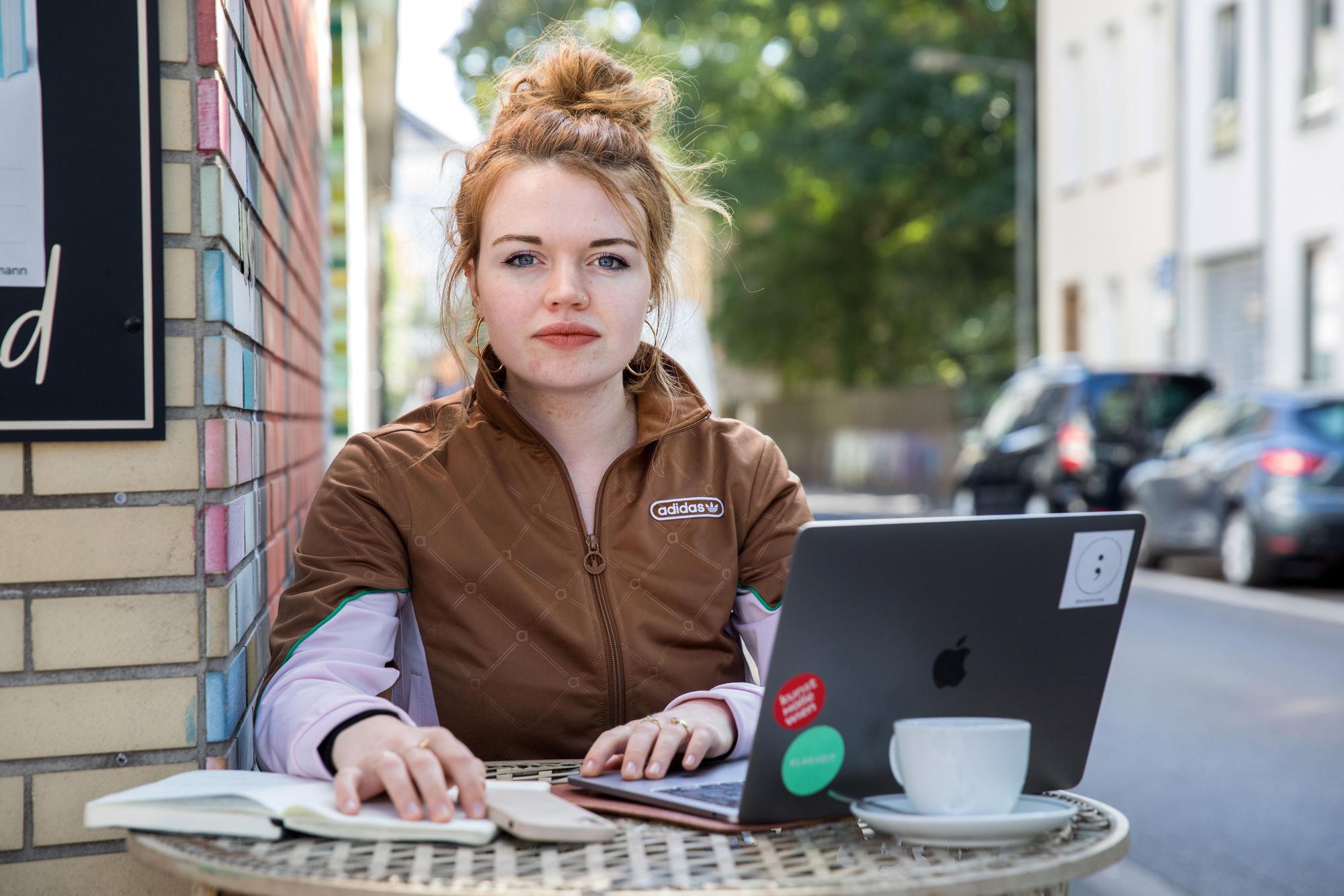 Autorin Maja Goertz sitzt mit Laptop und Schreibheft im Außenbereich eines Kölner Cafés.