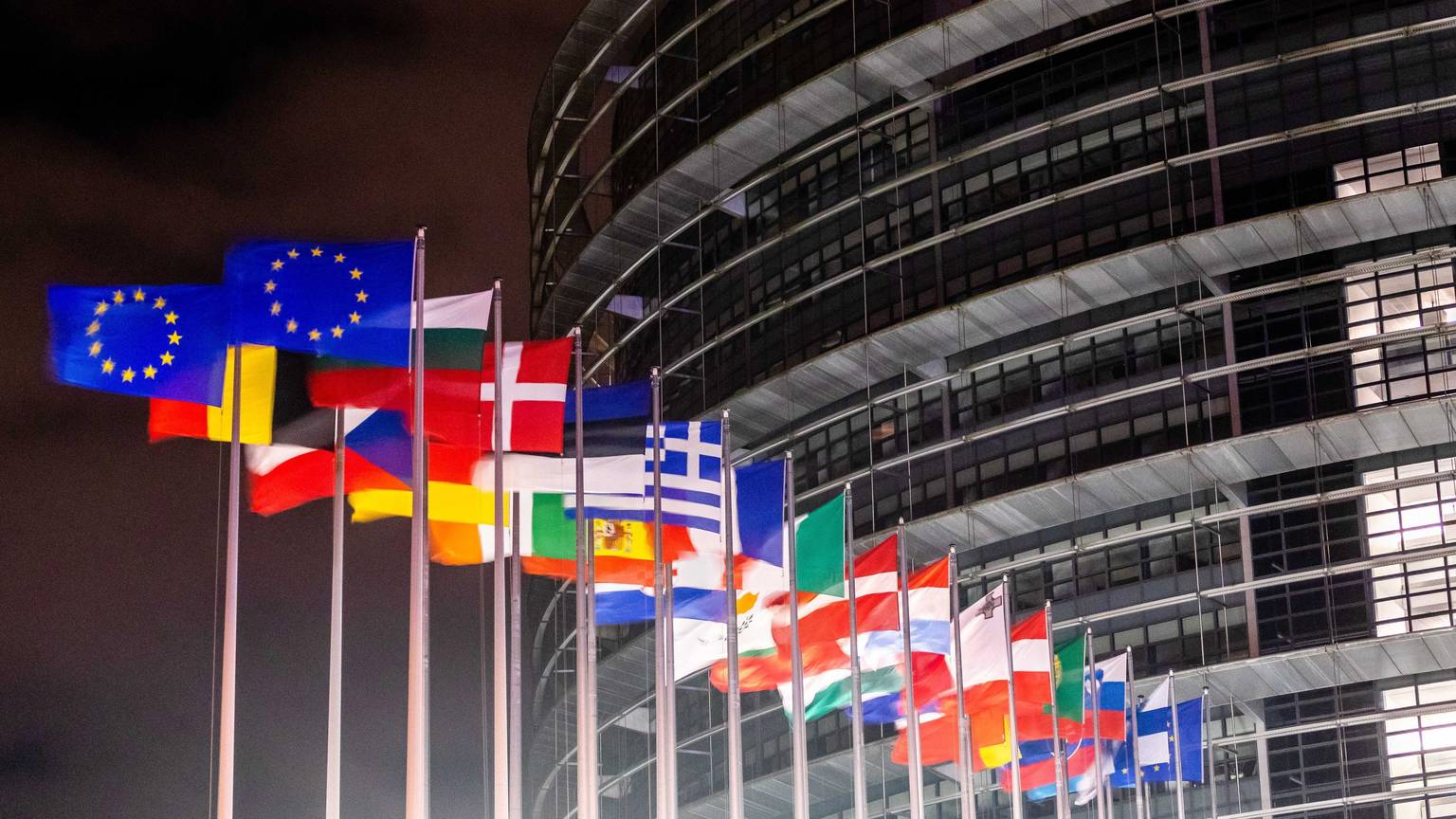 Das EU-Parlaments Gebäude im dunkeln. Flaggen stehen davor.