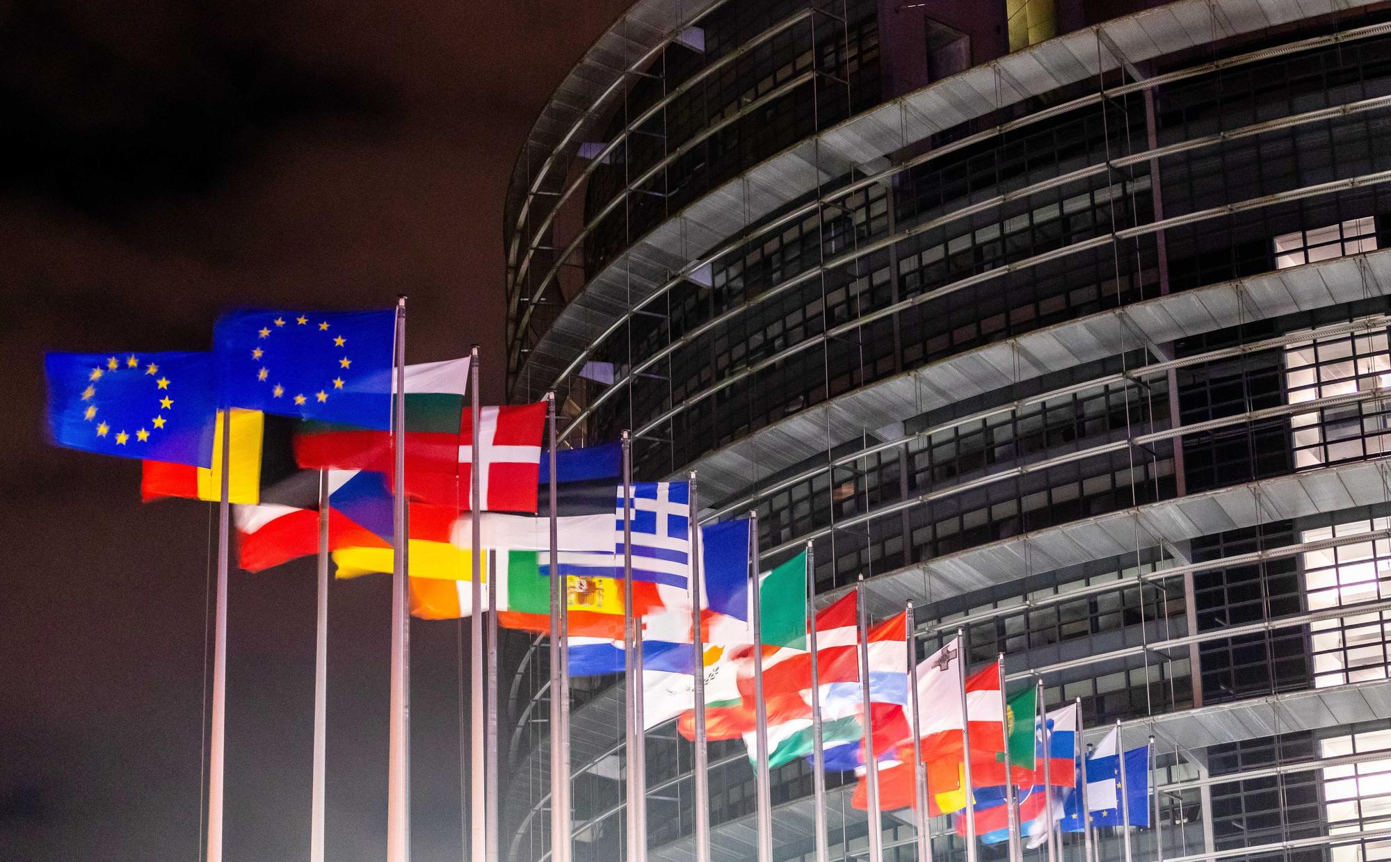 Das EU-Parlaments Gebäude im dunkeln. Flaggen stehen davor.