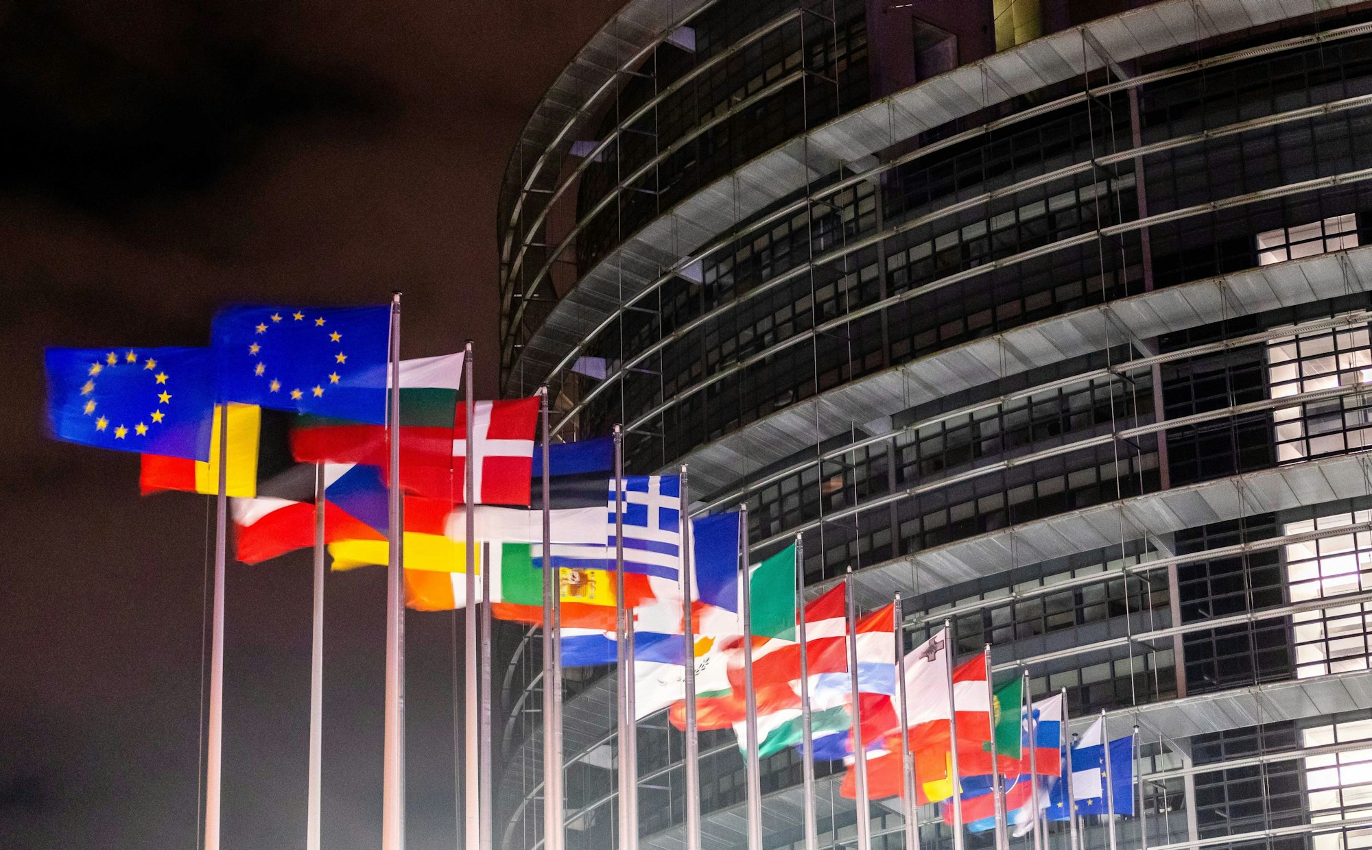 Das EU-Parlaments Gebäude im dunkeln. Flaggen stehen davor.